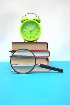 Green alarm clock and stack of books on blue table Stock Photos