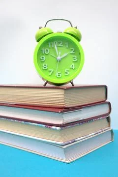 Green alarm clock and stack of books on blue table Stock Photos
