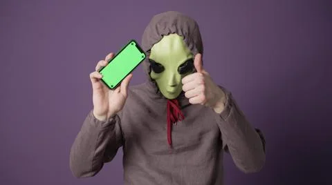 Green alien studies human technologies looking at phone Stock-Fotos