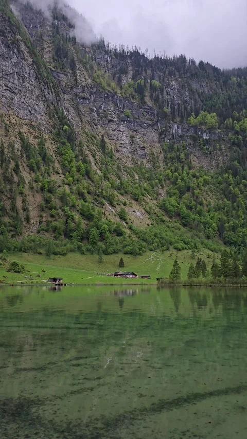Green alpine meadows and steep rocky slopes reflected in Lake Obersee.  Stock Footage 309029013