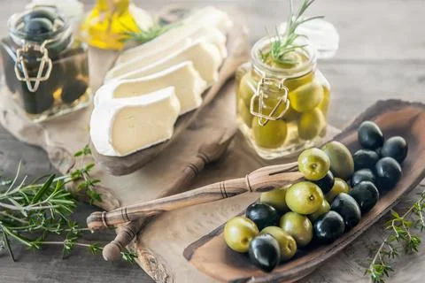 Green and black olives in glass jars with white soft brie cheese and young ol Stock Photos