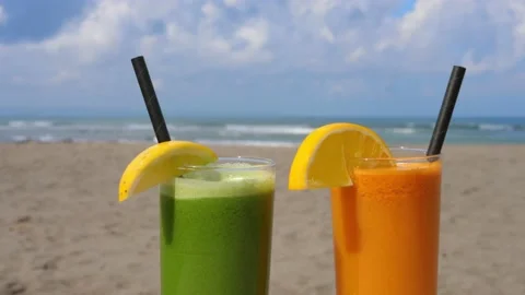 Green and orange refreshing tropical drinks in glasses on the sandy beach with Stock Footage 166074237
