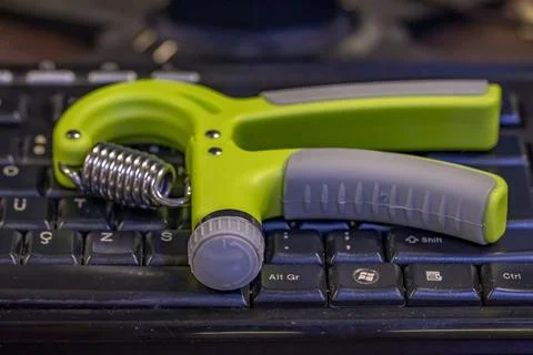 A green and silver hand exerciser sits on a keyboard Stock-Fotos