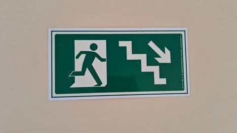 Green and white rectangular emergency exit sign pointing down stairs Stock Photos
