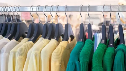 Green and yellow knitted sweaters hang on wooden hangers in clothing store. Stock Footage 307890970
