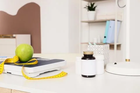 Green apple and measuring tape on a weight scale with supplement bottles, hea Stock Photos