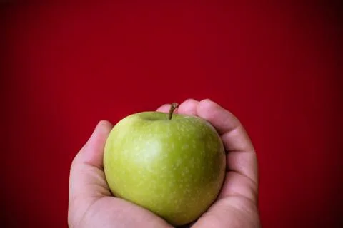 Green apple held by hand with red background. Stock Photos