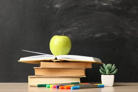 Green apple on open book with stack of books and colored markers Stock Photos
