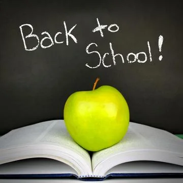 Green apple resting on open textbook against a blackboard with Back to Scho.. Stock Photos