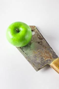 Green apple on a white background. An apple is standing on a kitchen hatchet. Stock Photos