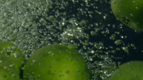 Green apples fall down in water against black background, super slow motion Stock Footage 97440262