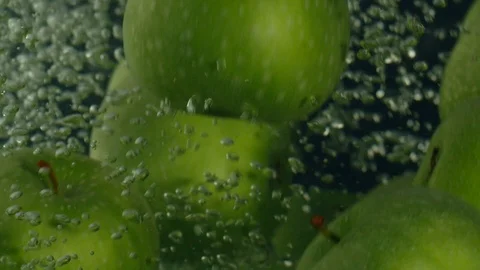 Green apples fall down in water against black background, super slow motion Stock Footage 97440322