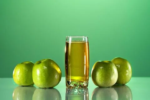 Green apples lie on the table with a reflection. next to it is a glass of apple Stock Photos