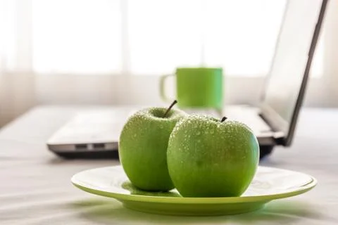 Green apples on a table with laptop near window Stock Photos