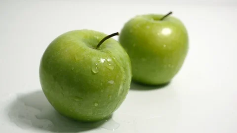 Green apples on white, splashed with drops of water. Slow zoom in. Stock Footage 99263343