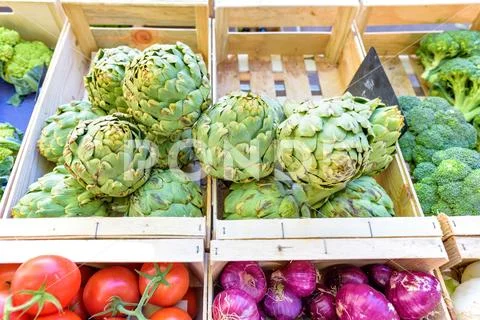Green Artichokes, red tomatoes, broccoli and onions in wood boxes for sale Stock Photos