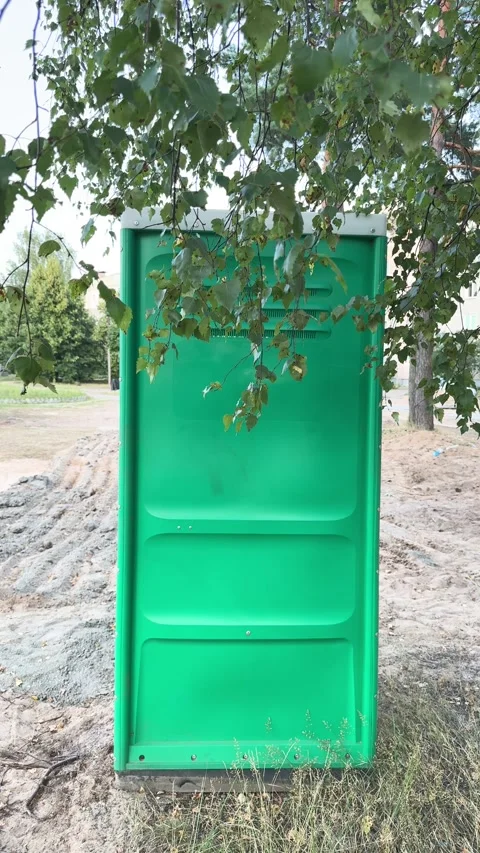 The green back panel of a portable toilet cabin stands on sandy ground  Video stock 341950167