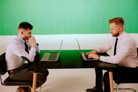 Green background studio two workers men wearing business clothes sitting on the Stock Photos
