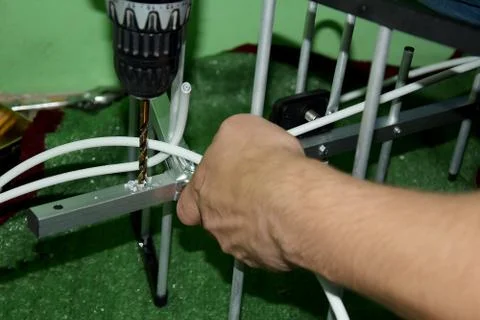 On a green background, surrounded by various spare parts, a man drills with a Stock Photos