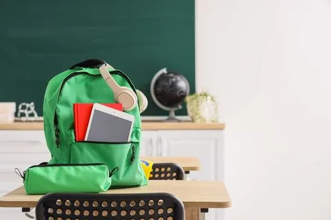 Green backpack with books, tablet, and headphones on a school desk in a class Stock Photos