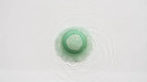 Green bath bomb ball dissolves in water with white foam bubbles. Cosmetic Stock Footage 253773005