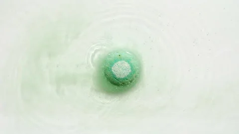 Green bath bomb ball dissolves in water with white foam bubbles. Cosmetic Stock Footage 254761747