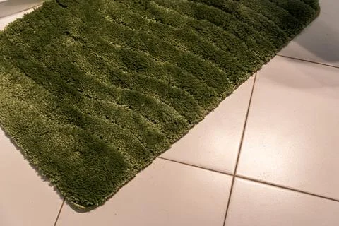 Green bath mat with textured wavy pattern placed on white ceramic tile floor in Stock Photos