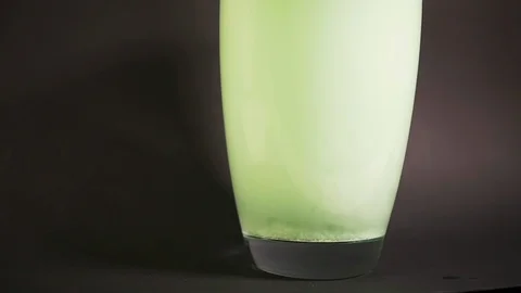 Green bath salt dissolves in vase of water in slow motion with particle drilling Stock Footage 119031269
