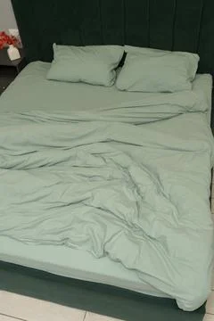 Green bedding set on unmade bed with pillows and headboard visible Stock Photos
