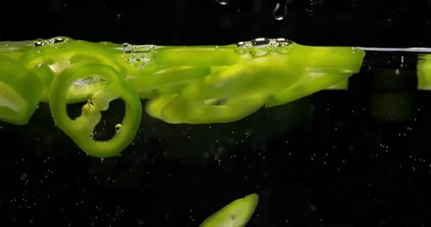 Green bell pepper slices fall down into water on black Stockbeeldmateriaal 145716295