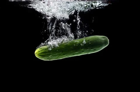 Green bio cucumber sinking under water against black background 库存照片