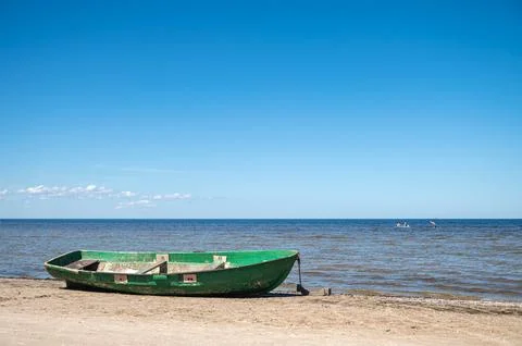 Green boat sits on sandy beach by water with few clouds in clear sky during d Stock Photos