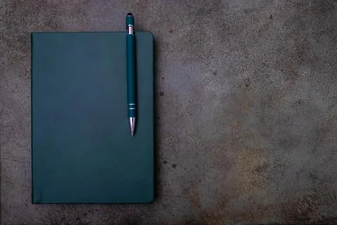A green bound notebook on a light brown, textured surface, accompanied by a pen Stock Photos