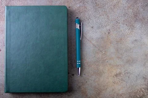 A green bound notebook on a light brown, textured surface, accompanied by a pen Stock Photos