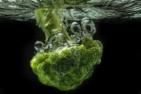 Green broccoli falling in water with splash on black with air bubbles Stock Photos