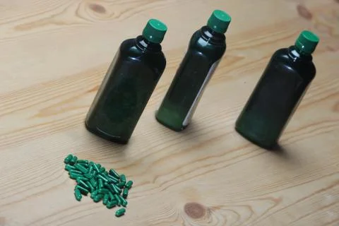 Green capsule heap and three green syrup bottle Stock Photos