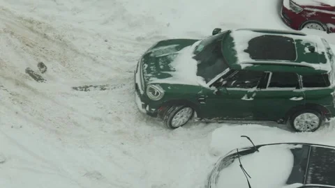 Green car stuck in deep snow drift with wheels spinning attempting to move on Video stock 342230945