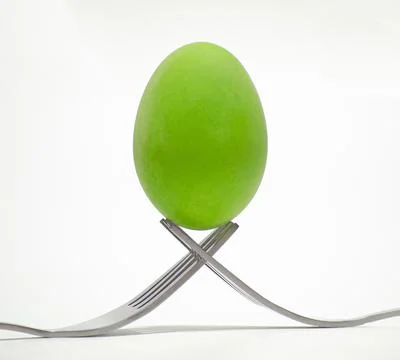 A green chicken egg is placed on the tip of a cutlery. Stock Photos