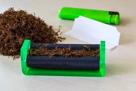 Green cigarette rolling machine, cigarette paper, green lighter and tobacco Stock Photos