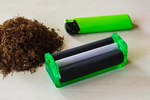 Green cigarette rolling machine, green lighter and pile of tobacco on a table Stock Photos