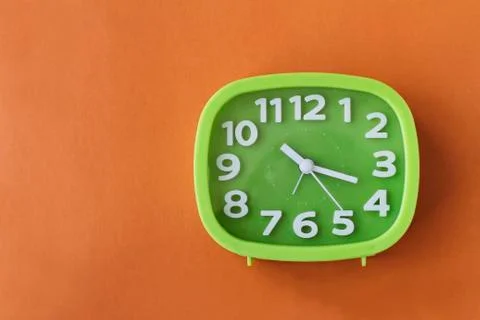 Green clock with white numbers and arrows on orange background Stock Photos