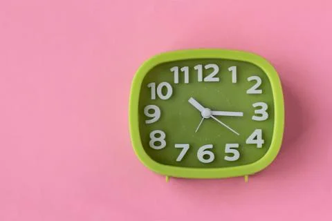 Green clock with white numbers and arrows on pink background Stock Photos