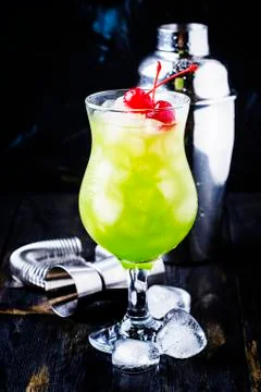 Green cocktail with maraschino cherries in a hurricane glass, dark background Stock Photos