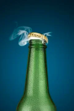 Green cold beer bottle with water drops and golden cap open on blue background Photos