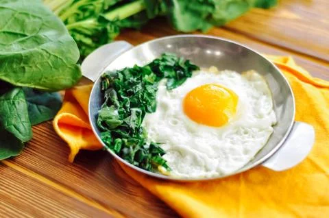 Green cooked spinach with fried egg on iron pan plate. Fried eggs healthy Stock Photos