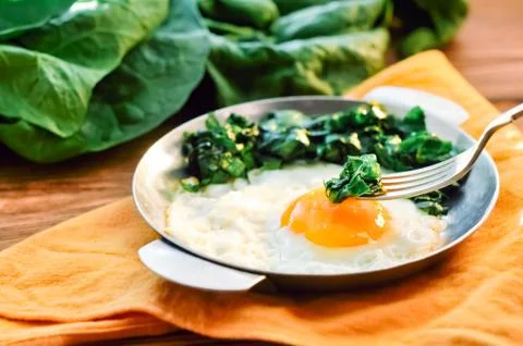 Green cooked spinach with fried egg on iron pan plate. Fried eggs healthy Stock Photos