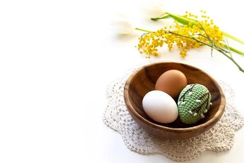 Green crocheted Easter egg and chicken eggs in a wooden plate on a white back Stock Photos