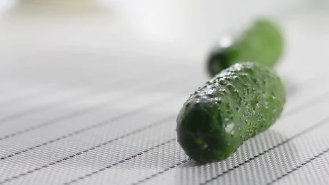 Green cucumber lies on a white table. A cucumber rolls in the background Stock Footage 124190491