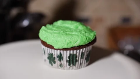 Green cup cake with four leaf clovers sliding across white plate slow motion Video stock 150607420