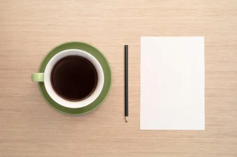 A green cup of coffee on the background of a table and a white shee and penci Stock Photos
